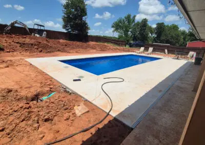 Rectangular in-ground pool with concrete deck amid new backyard construction