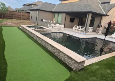 Backyard modern pool with raised stone spa and artificial turf
