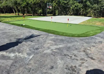 Concrete driveway and backyard putting green with three red flags