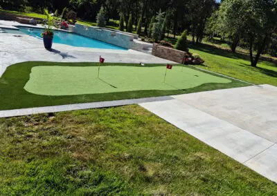 Backyard artificial putting green with three numbered flags beside a pool