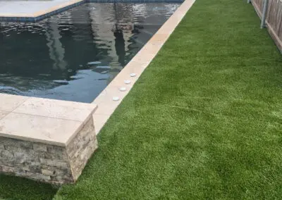 Artificial turf lawn beside modern backyard pool with patio seating