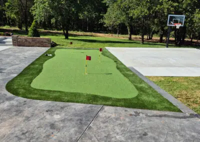 Backyard synthetic putting green with three flags next to basketball court