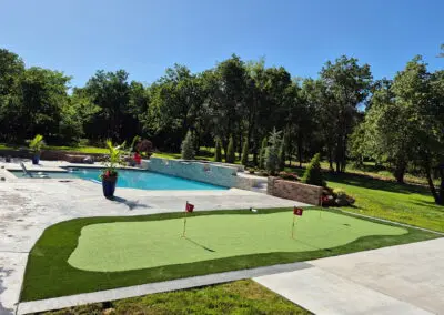 Backyard putting green beside a custom swimming pool and landscaped yard