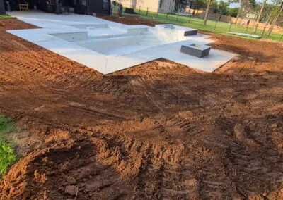 Backyard construction site with newly poured concrete pool shell and surrounding dirt