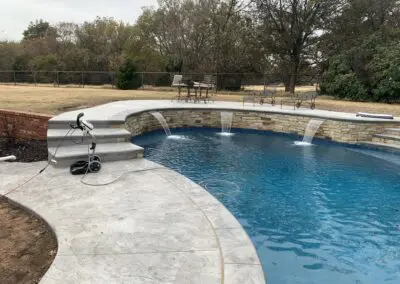 backyard pool with three stone water spouts and stamped concrete deck