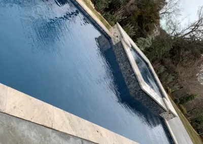 Rectangular backyard pool with raised spa, stone coping, concrete deck, winter trees