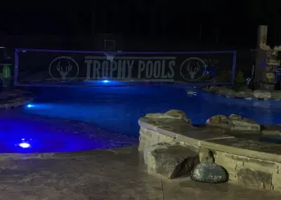 Night pool with blue LED lights and "Trophy Pools" banner across water