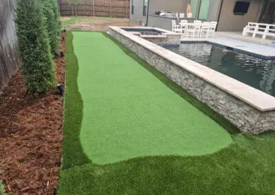 Backyard artificial turf putting green beside pool and stone retaining wall