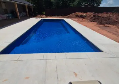 Rectangular backyard concrete pool with bright blue water and lounge chair