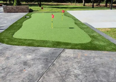 Concrete driveway and backyard putting green with three red flags