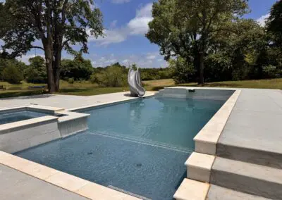 Modern rectangular backyard pool with spa, slide, and surrounding patio