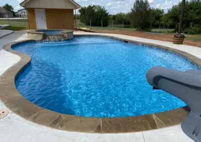 Residential freeform blue pool with spillover spa and concrete deck