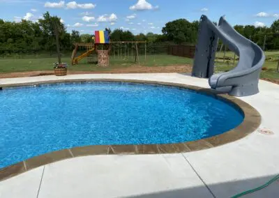 Backyard blue swimming pool with concrete deck, stone coping, and slide