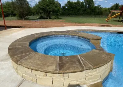 Round stone spa and pool with textured coping and clear blue water