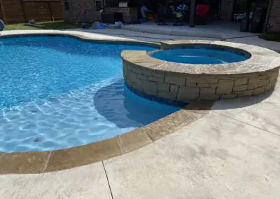 Backyard blue swimming pool with raised stone hot tub and concrete deck