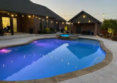 Backyard illuminated freeform pool and raised spa with string lights