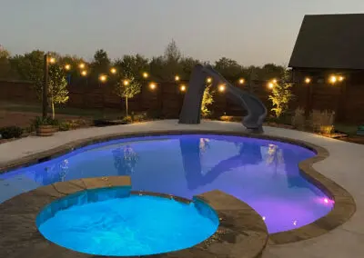 Backyard freeform pool and illuminated spa with slide and string lights