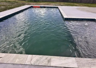 Residential rectangular backyard pool with greenish water and concrete deck