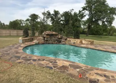 Backyard freeform swimming pool with stone coping and rock waterfall