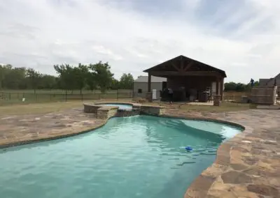 backyard freeform swimming pool with spa, stone decking, and covered patio