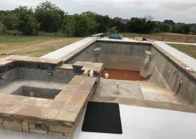 Empty backyard inground pool shell under construction with raised spa