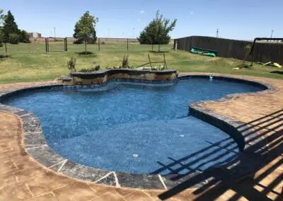 Backyard freeform blue swimming pool with stamped concrete patio and water feature