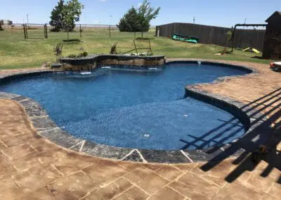 Backyard freeform blue swimming pool with stamped concrete patio and water feature