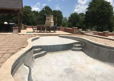 Empty concrete backyard pool under construction with tiled steps and patio seating