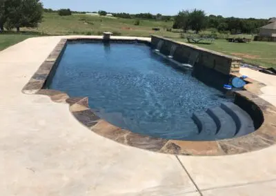 Backyard custom pool with stone coping, spillway wall, and concrete patio
