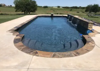 Residential backyard pool with stone coping, built-in steps, and three waterfalls