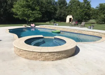 Backyard pool and raised spa with stone veneer and concrete deck
