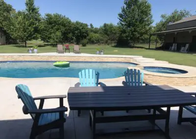 Backyard pool with hot tub, patio table and blue Adirondack chairs