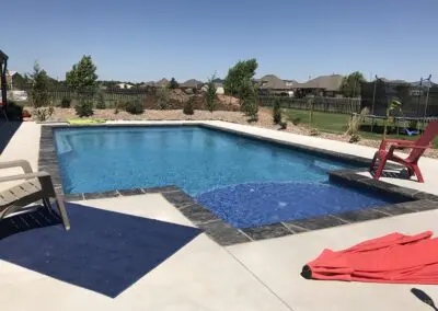 Backyard inground pool with spa, stone coping and patio chairs