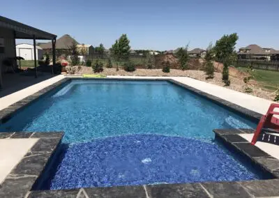Residential backyard rectangular pool with built-in spa and concrete deck
