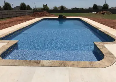 Backyard in-ground swimming pool with clear blue water and concrete deck