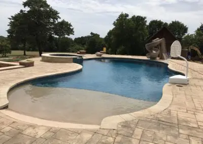 Backyard freeform pool with tanning ledge, spa, slide, and basketball hoop