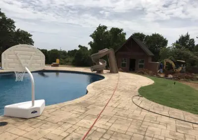 Residential pool patio with basketball hoop and slide near brick pool house