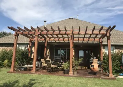 Backyard brick house patio with wooden pergola, outdoor chairs, and chiminea