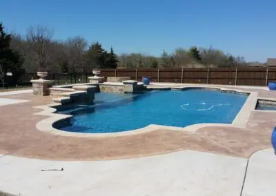 Backyard custom shaped swimming pool with stamped concrete decking and blue planters