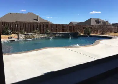 Backyard freeform pool with stone waterwall and concrete patio