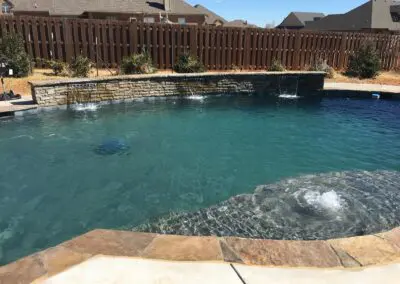 Backyard swimming pool with stone spillway and bubbling tanning ledge