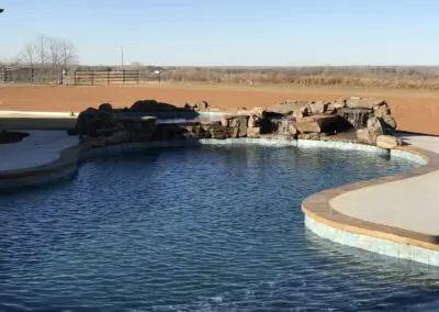 Backyard freeform swimming pool with rock waterfall and concrete decking