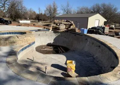 Empty in-ground pool under construction with stone coping and nearby workshop
