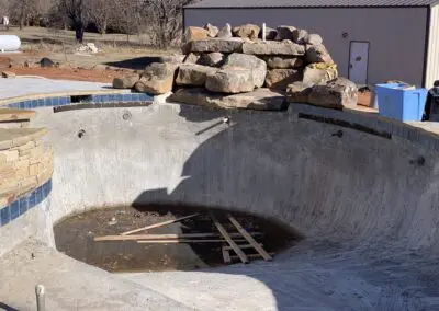 Empty concrete pool under construction with rock waterfall and scattered lumber