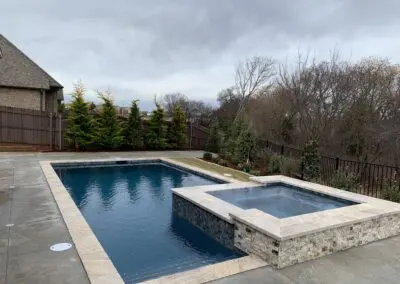 Backyard modern pool with raised spa and stone coping under cloudy sky