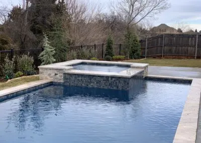 Backyard modern pool with raised spa and stone coping under cloudy sky