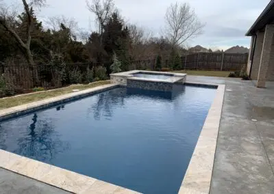 Backyard modern pool with raised spa and stone coping under cloudy sky