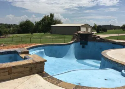 Empty blue plaster backyard pool under construction with stone coping and waterfall