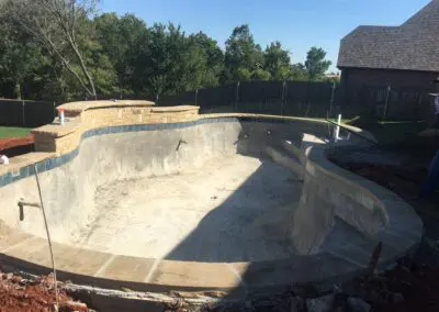 Empty backyard concrete pool shell under construction with stone coping