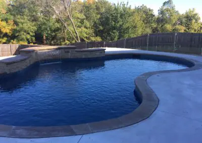 Backyard freeform blue swimming pool with stone spa and waterfall